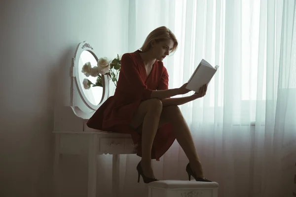 Изучает поэзию. сексуальная женщина изучает поэзию сидя в спальне. изучает поэзию дома. девушка в красном платье изучает поэзию. страстный читатель . — стоковое фото