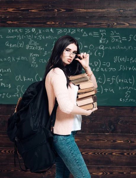 Portret van jonge brunette student met hoopje van boeken en zware rugzak holding haar bril — Stockfoto