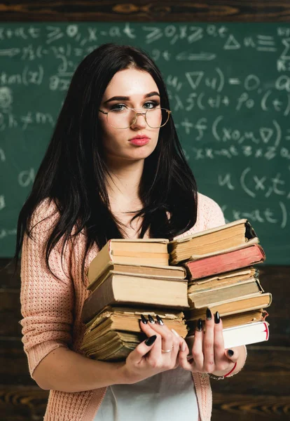 She loves reading. Girl bookworm take books in library. Student excellent fond of reading. Diligent student preparing for exam test. Girl nerd holds heavy pile of old books, chalkboard background