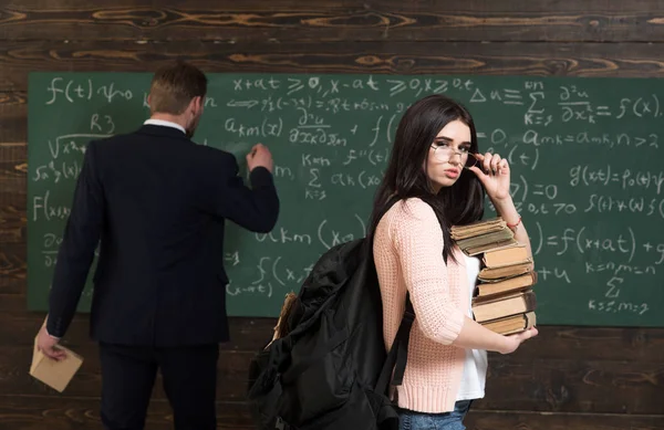 Ik hou om te studeren. Vrouw student kijken in de glazen met boek stack en rugzak met leraar man schrijven op schoolbord op school. Voorbereiding op het examen. She's got boeken die ze nodig heeft. Vertrouwen in kennis — Stockfoto