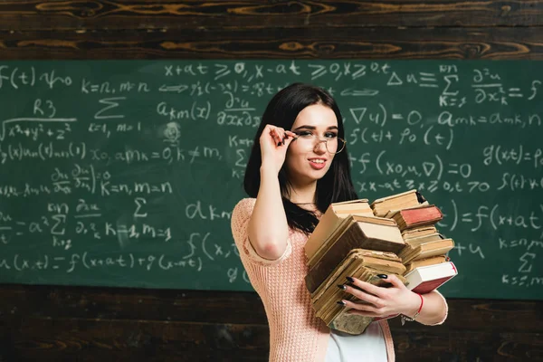 Curso de proyecto. Chica estudiante trabaja en el proyecto del curso. Estudiante excelente aficionado a studying.Girl sostiene pila pesada de libros antiguos, fondo de pizarra. Estudiante diligente preparándose para la prueba de examen — Foto de Stock