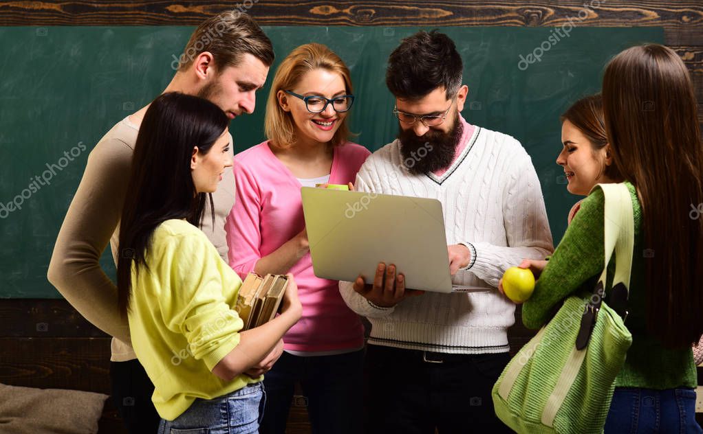 College and university concept. Group of students, groupmates spend time with teacher, lecturer, professor. Students, scientists studying after classes, professor holds laptop, teaches , explaining.