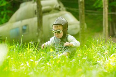 Çocuk ve doğal zemin üzerine bulanık helikopter. Seyahat ve macera. Mutlu çocukluk kavramı. Pilot kask ve gözlük yeşil çim oturan çocuk. Oynama ve rüya.