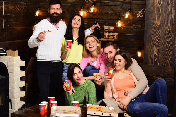 Students pizza party concept. Youth celebrate with drinks and pizza, spend time together, speaking. Students, friends, group mates with teacher celebrate, have fun, dark wooden interior background