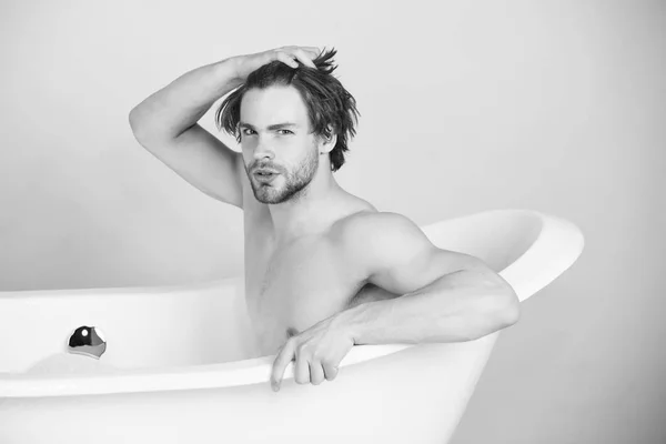Handsome young man with muscular body sitting in white bathtub — Stock Photo, Image