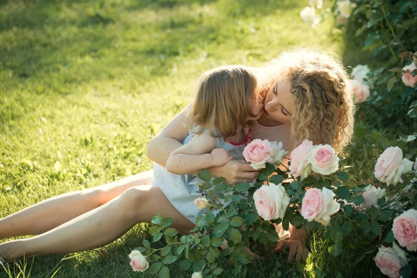 Mamma kysser dotter på grönt gräs på solig sommardag — Stockfoto