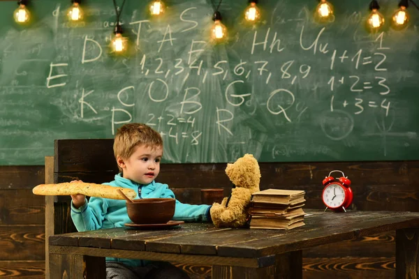 Школьник наслаждается обедом с другом-игрушкой в классе. Школьник ест еду с плюшевым мишкой на деревянном столе. Школьник ужинает. Здоровое меню для школьника. Smart is great — стоковое фото