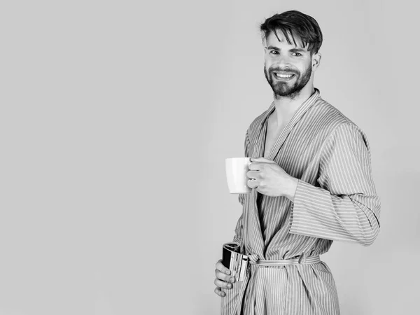 Человек улыбается в халате с чашкой и журналом — стоковое фото