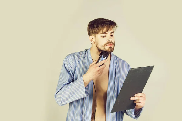 Bearded man in blue robe shaving beard with electric shaver — Stock Photo, Image