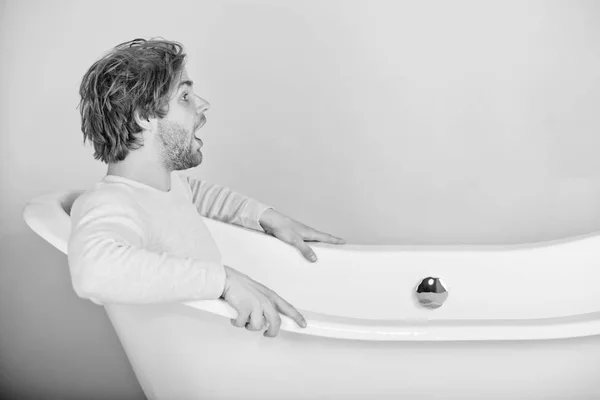 handsome young surprised man in underwear sitting in white bathtub on pink background, spa and beauty, relax and hygiene, healthcare, copy space