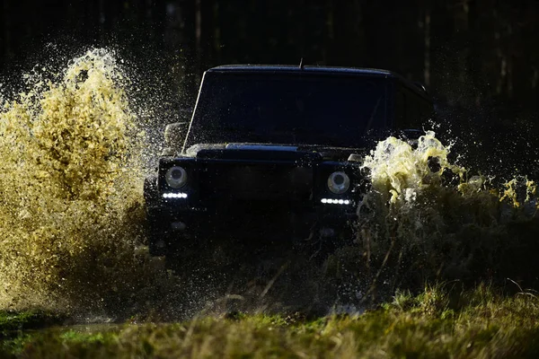 Offroad race op val natuur achtergrond. Extreme, uitdaging en 4 x 4 voertuig concept. SUV of offroad auto op pad bedekt met gras overschrijding van de plas met water splash. Auto race in herfst bos — Stockfoto