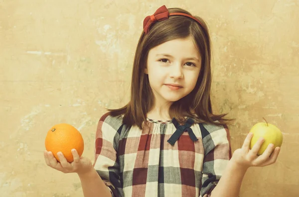 Kind of girl bedrijf van sinaasappel en appel in handen — Stockfoto