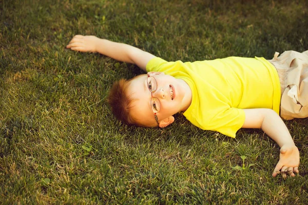 Happy baby boy z rude włosy w okularach na trawie — Zdjęcie stockowe
