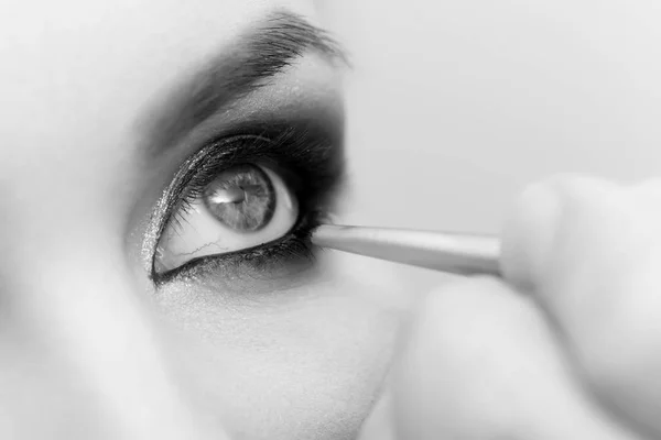 Olho de mulher recebendo maquiagem contorno com sombra preta e escova — Fotografia de Stock