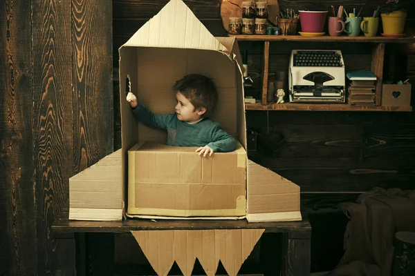 Niño sentado en cartón cohete hecho a mano. Concepto de infancia. Chico jugar en casa con cohete, pequeño cosmonauta sentarse en cohete hecho de caja de cartón. Niño jugar cosmonauta, astronauta . —  Fotos de Stock