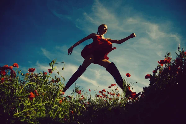 Opium, Frau oder springendes Mädchen mit langen lockigen Haaren im schwarzen Body und Kleid im roten Blütenfeld aus Mohn mit grünem Stiel auf blauem Himmelshintergrund, Sommer, Drogen- und Liebesrausch, Opium — Stockfoto