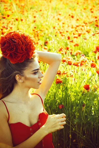 Женщина или девушка с длинными вьющимися волосами в красном платье держат цветочный букет в поле маковых семян с зеленым стеблем на естественном фоне, летом, весной, наркотиками и любовью интоксикации, опиум — стоковое фото
