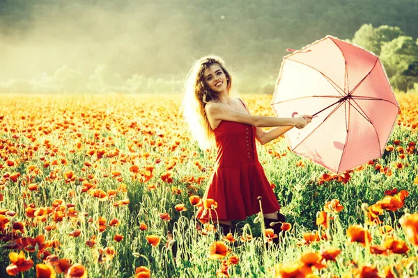 Paraply rosa färg på ganska glad tjej med långt lockigt hår i röd klänning i fältet vallmofrö blomma på grön stam på naturlig bakgrund, sommar, drog- och kärlek berusning, opium — Stockfoto