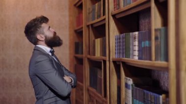 Takım elbiseli bir adam kitaplığındaki kitaplık önünde duruyor ve bir kitap seçer. Kütüphane kavramı.