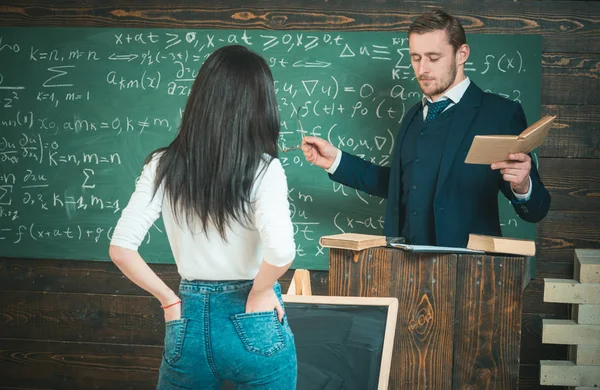 Уверенный профессор дает объяснения, держа в руках книгу и очки. Вид сзади девушка с руками в карманах джинсов — стоковое фото