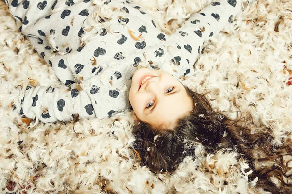 Söt glad tjej på golvet täckt med ner och fjäder — Stockfoto