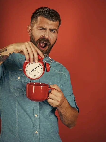 man with beard on sleepy face with cup, alarm clock