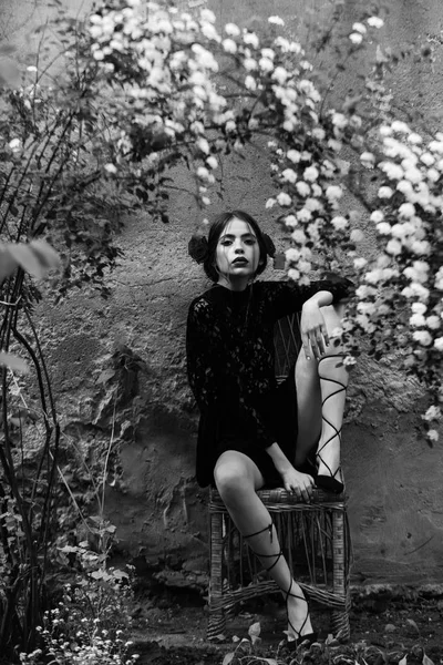 Mulher bonito em preto, vestido de renda sentado na cadeira de vime — Fotografia de Stock