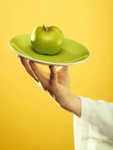 Pomme verte sur assiette en main du jeune chef en manche blanche sur fond jaune — Photo