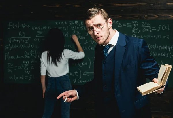 Teacher holding a book in front of a chalkboard looking surprised — Stock Photo, Image