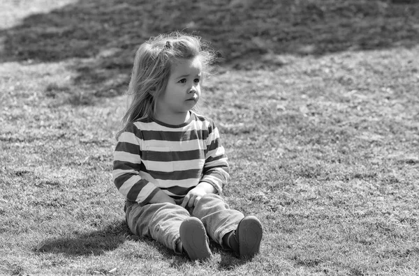 Aranyos kisfiú ül a zöld gyep a parkban — Stock Fotó