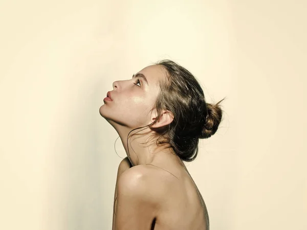 Girl with hair bun, nude shoulders look up on white background