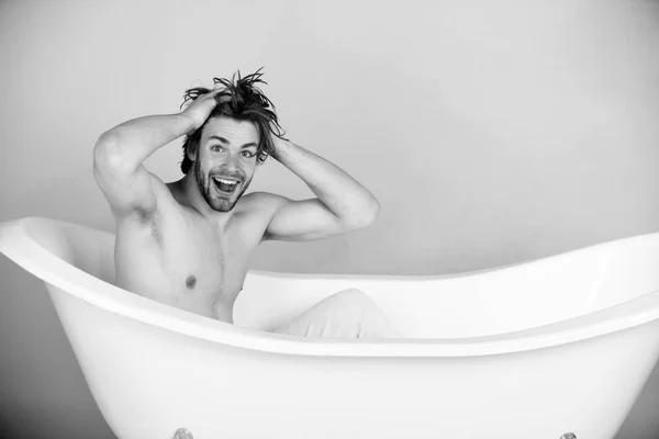 Joven guapo con cuerpo musculoso sentado en bañera blanca —  Fotos de Stock
