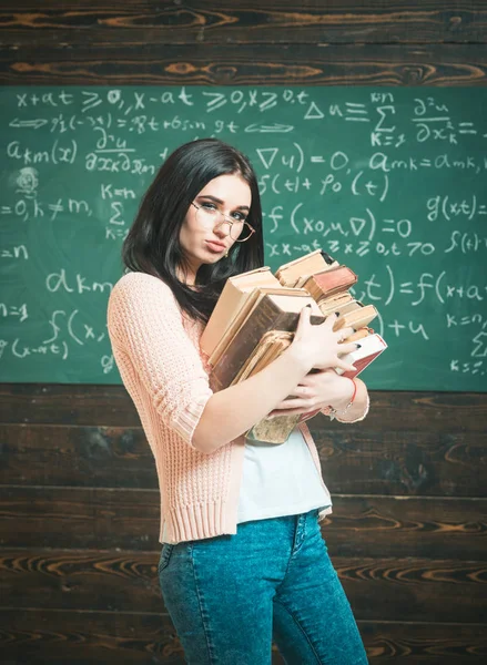 Brunette female student in classroom. Sexy young college girl walking with two heaps of books