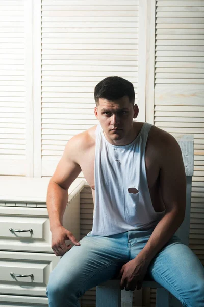 Young man sit on chair. Guy in trendy tank top and jeans fashion. Athletic macho with muscular chest and hands. Fashion model with stylish hair. Mens fashion style and trend — Stock Photo, Image