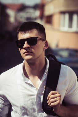 Yakışıklı şık beyaz adam omuzlarında sırt çantası ile sokak arka plan karşı poz trendy güneş gözlüğü takıyor. Gezgin adam şehirde. Yaşam tarzı moda kentsel kavramı