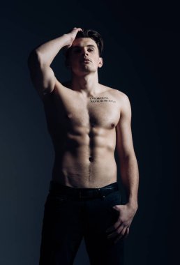 Gövde, altı paketleri, koyu arka plan ile kas maço adam. Adam dövme ile kendinden emin ve çekici görünüyor. Maço kas şekil, sporcu, vücut geliştirmeci dalgın yüzünde. Seksi maço kavramı.