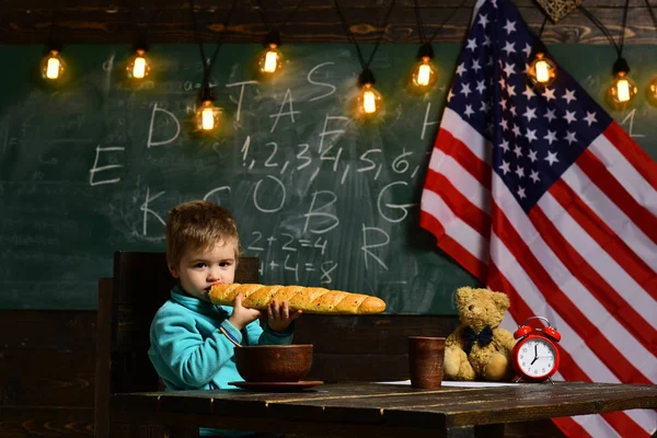 Patriotismo y libertad. Niño de la escuela en la clase del 4 de julio. De vuelta a la escuela o a la escuela en casa. El niño come pan en la bandera americana en el día del conocimiento. Feliz día de la independencia de los EE.UU. —  Fotos de Stock