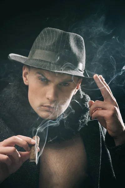 老式侦探概念。穿大衣的男人, 抽雪茄的帽子, 深色的背景。穿着老式衣服的家伙看起来很神秘, 雪茄和烟雾。神秘面孔的男子汉, 侦探, 侦探, 探员. — 图库照片