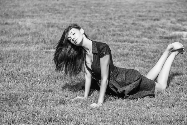 若いセクシーな女性または長い髪と緑の草晴れた日の屋外自然な背景の上に黒い夏ドレス Layng のきれいな顔の女の子 — ストック写真