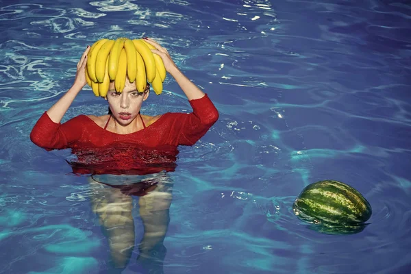 Plátano y sandía en la cabeza de la mujer. El plátano y la sandía la fruta fresca a la muchacha en el agua de piscina — Foto de Stock