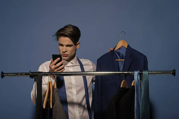 Бизнесмен использует мобильный телефон в гардеробе на синем фоне — стоковое фото
