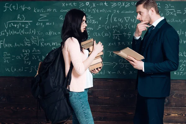 Estudante vista lateral e professor tendo uma discussão. Menina com mochila pesada e pilha de livros em suas mãos em pé professor oposto que está tocando sua barba — Fotografia de Stock