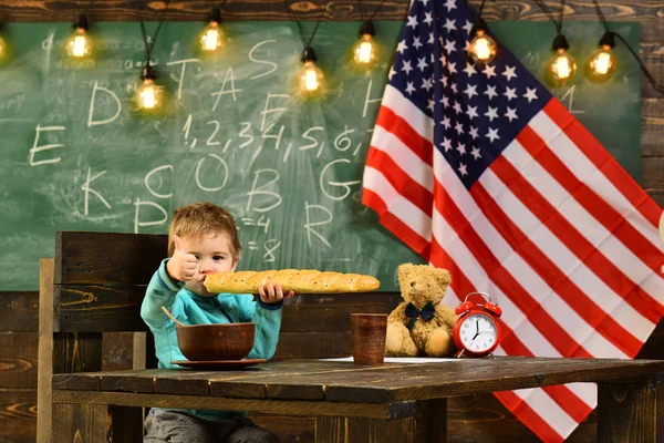 El niño come pan en la bandera americana en el día del conocimiento. De vuelta a la escuela o a la escuela en casa. Feliz día de la independencia de los EE.UU. Patriotismo y libertad. Niño de la escuela en la lección del 4 de julio —  Fotos de Stock