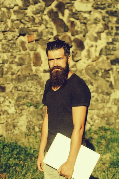 Bearded man with long beard standing with grey laptop