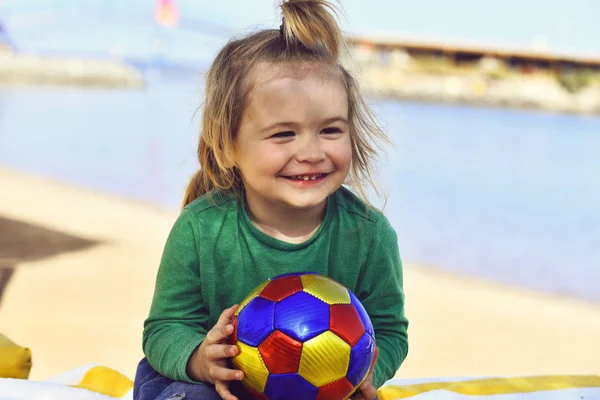 Pequeño niño sonriente con pelo largo y rubio sosteniendo la pelota —  Fotos de Stock