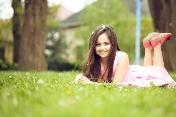 Kleines Mädchen auf grünem Gras mit Blütenblättern — Stockfoto