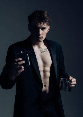 Lüks alkol kavramı. Maço emin yüz, kas şekil, şişesi ile alkol ve metalik Kupası tutar. Kas gövde, altı paketleri, adamla klasik ceket giyer, çekici, koyu arka plan görünüyor