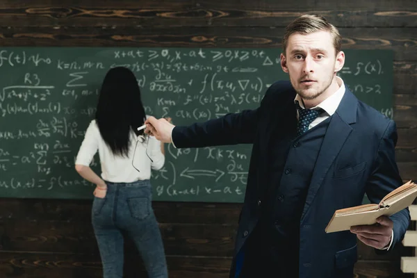 Aufgeregter junger Professor zeigt auf grüne Tafel mit viel Schrift einer Studentin in weißem Pullover und blauer Jeans — Stockfoto