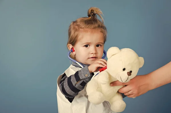 Мальчик-врач осмотреть игрушечного питомца со стетоскопом на синем фоне — стоковое фото