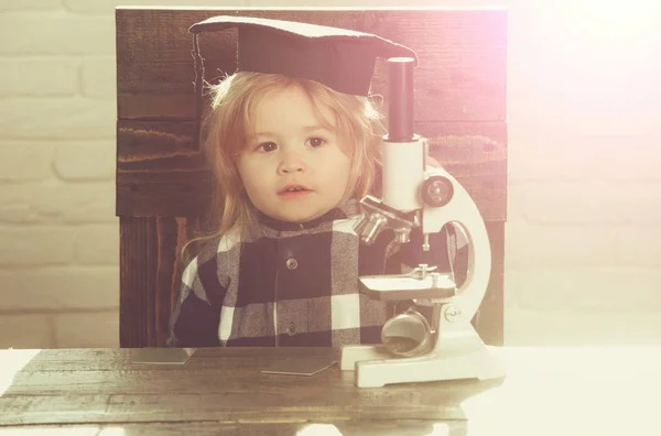 Menino pequeno, criança cientista em chapéu de graduação com microscópio — Fotografia de Stock